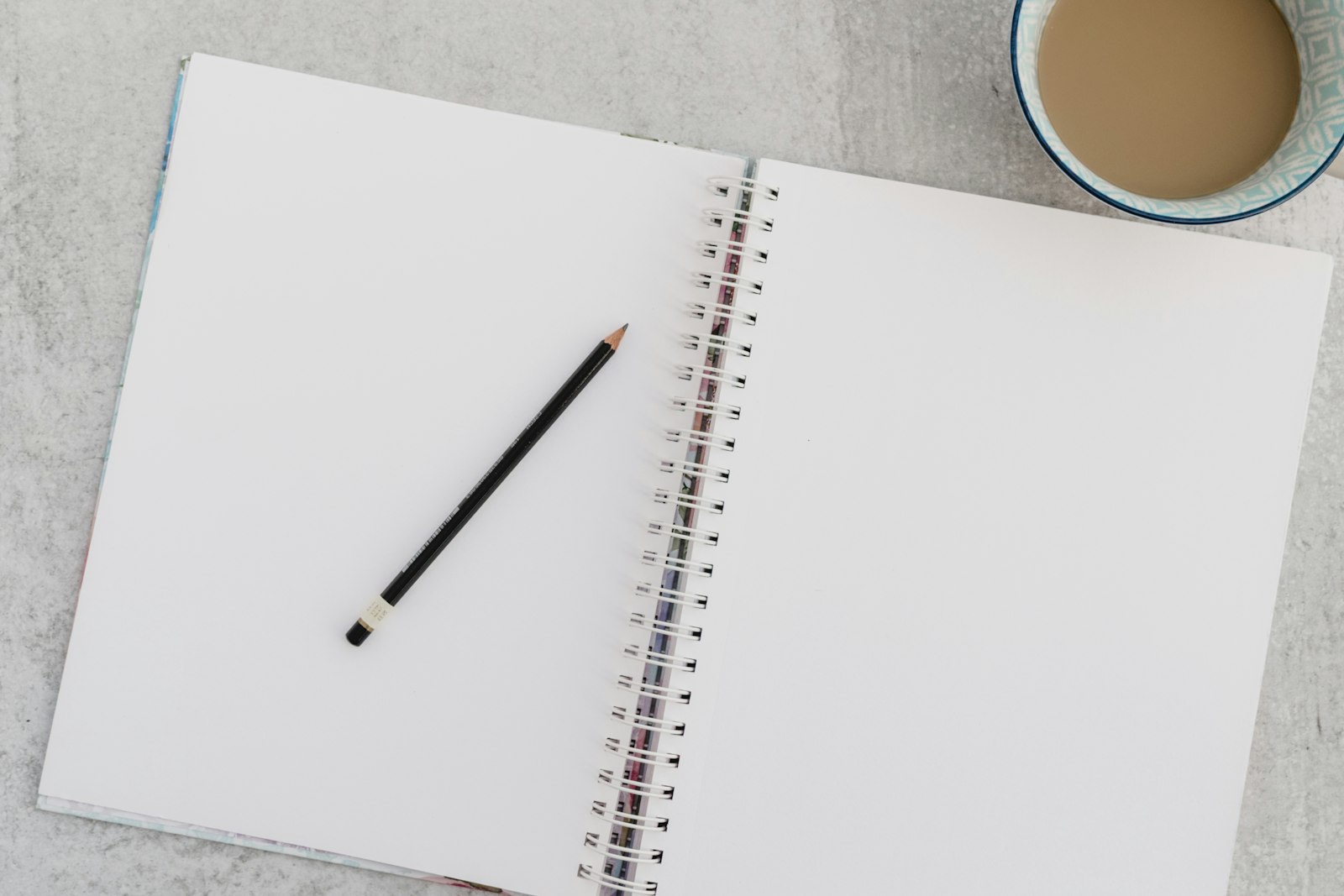 An open notebook and pencil beside a cup of coffee